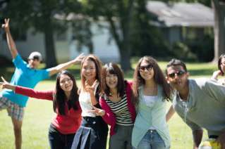 A group photo of six smiling college students pose for a picture together outside on a sunny day.