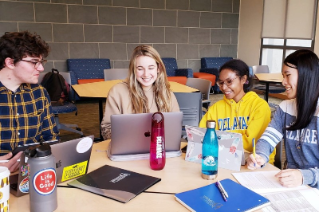 Four students sitting with laptops wearing University of Delaware group at a table in conversation