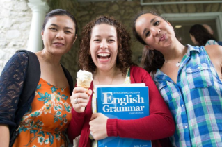 Three female students smiling, one is holding an ice cream cone and an English grammar book