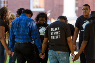 Group of African American students standing in a circle holding hands with heads bowed down