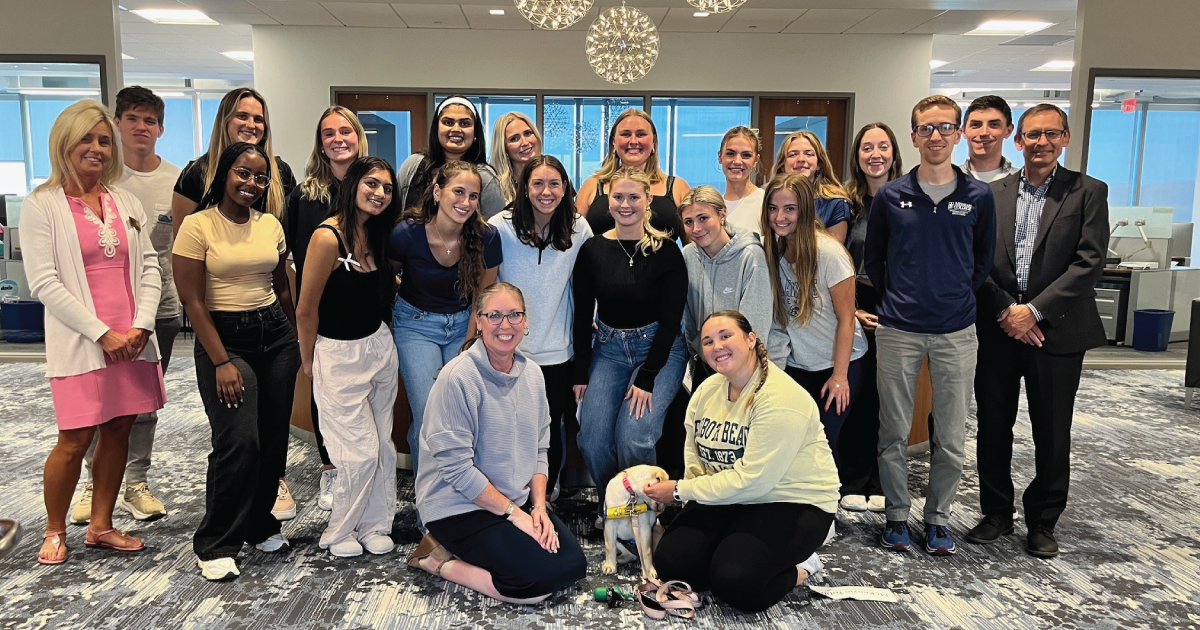 Group of college students and staff gathered around with a dog for a group photo