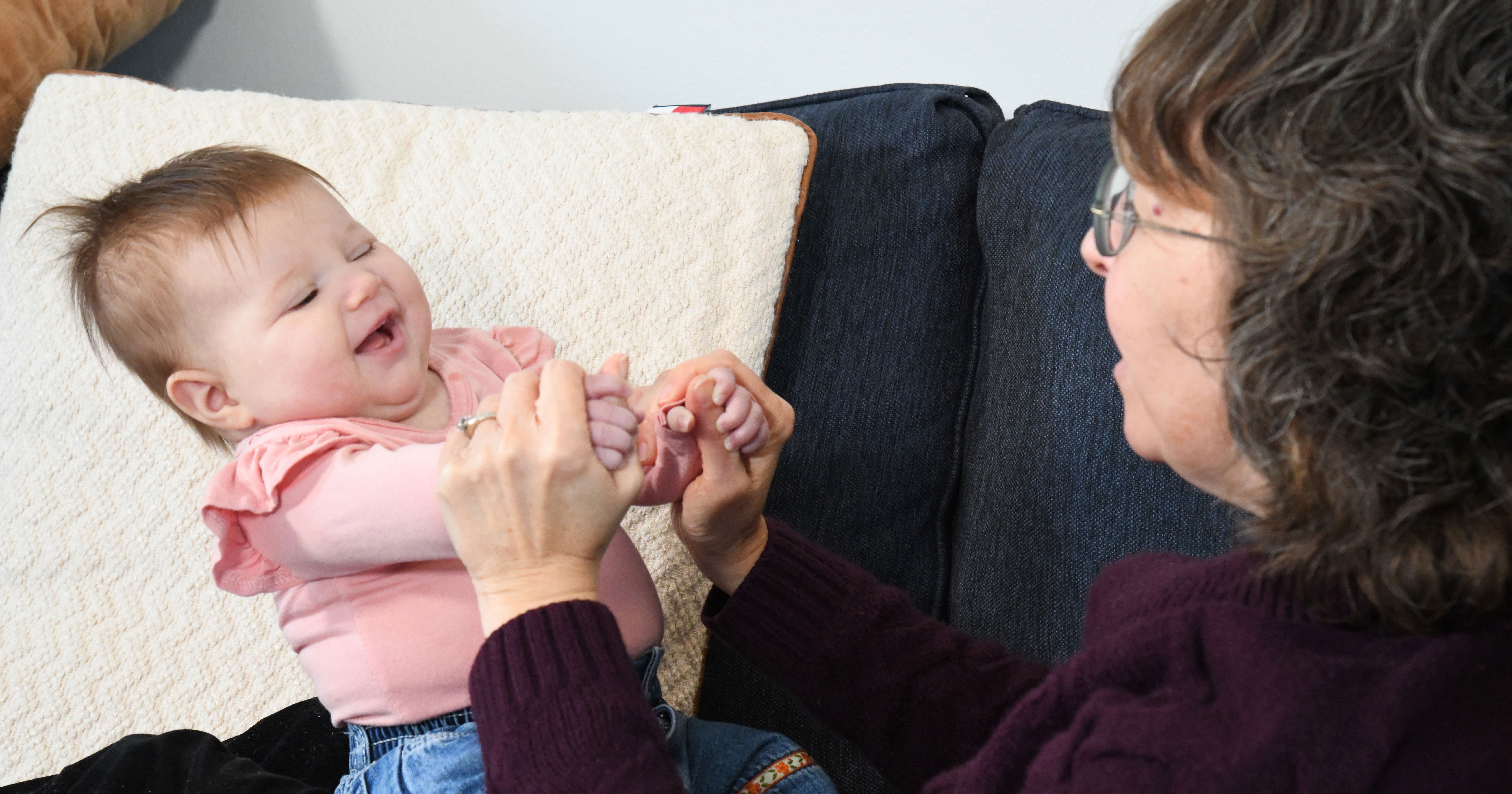 A baby is smiling while Associate Professor of Physical Therapy Michele Lobo plays with the infant's hands, holding them, as baby grips back.