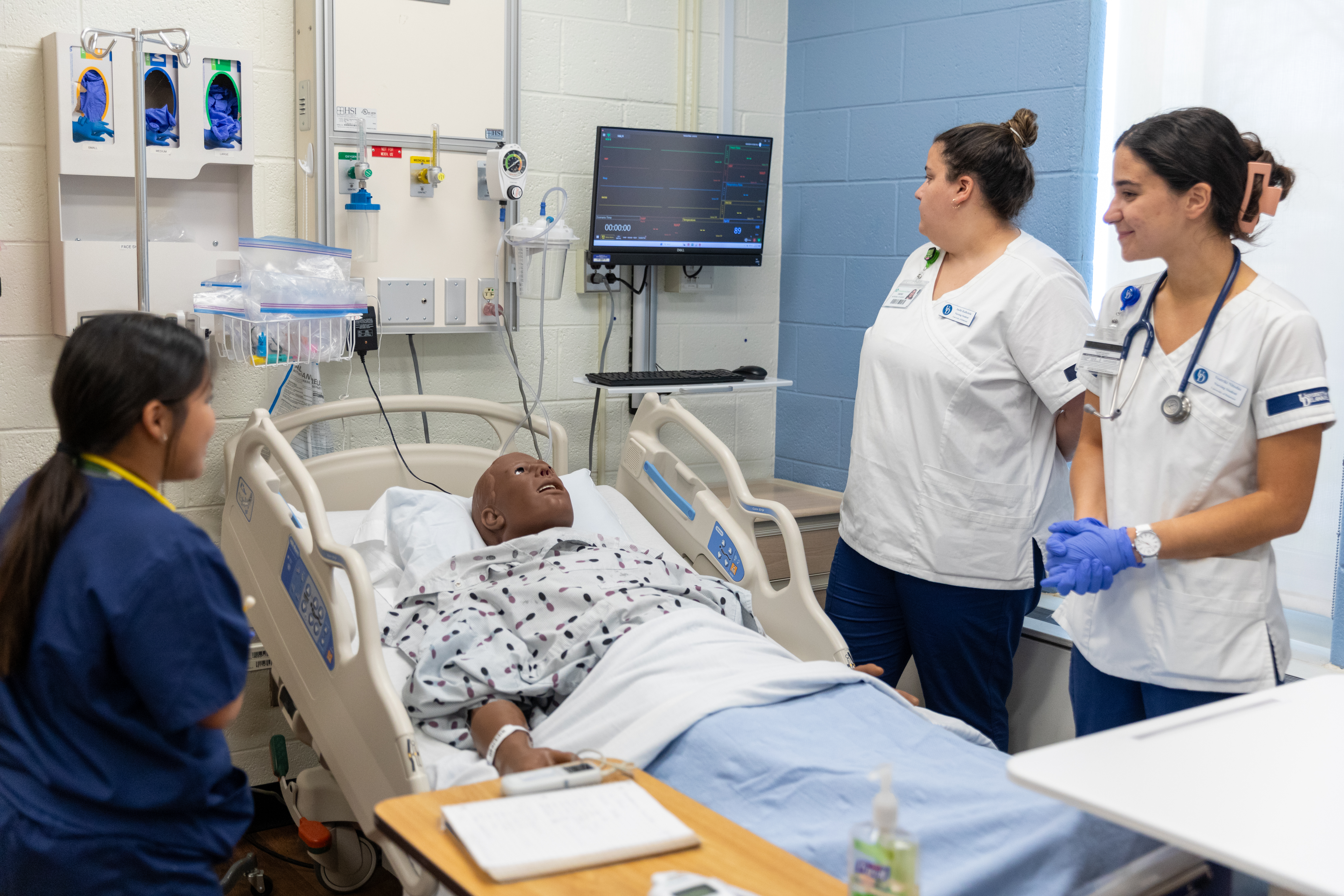 Nursing students an faculty gathered around a test patient in a hospital bed