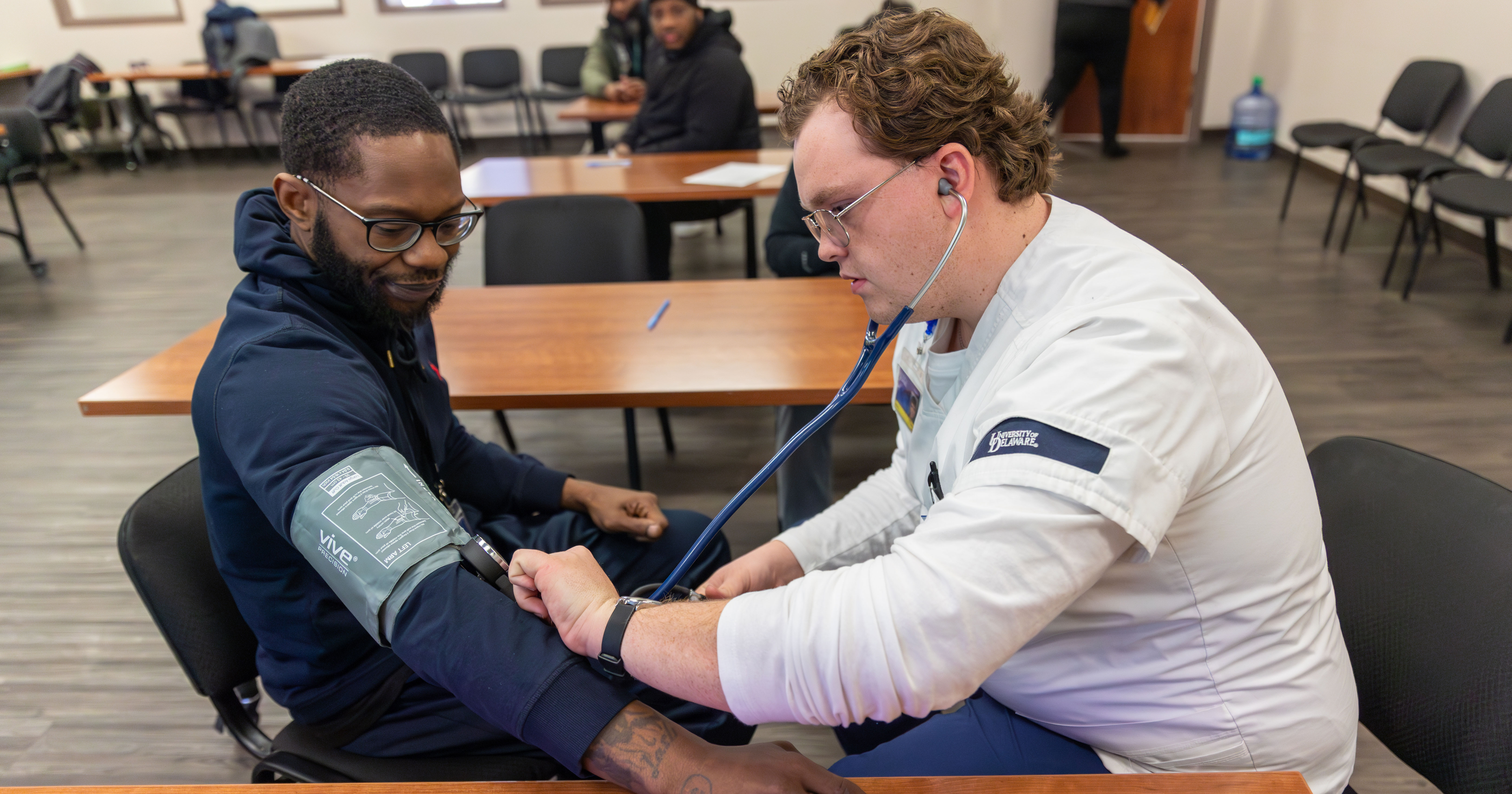 Senior nursing major David Metcalf checks a man's blood pressure, using a blood pressure cuff during a peer therapy group meeting at the Wilmington HOPE Commission.