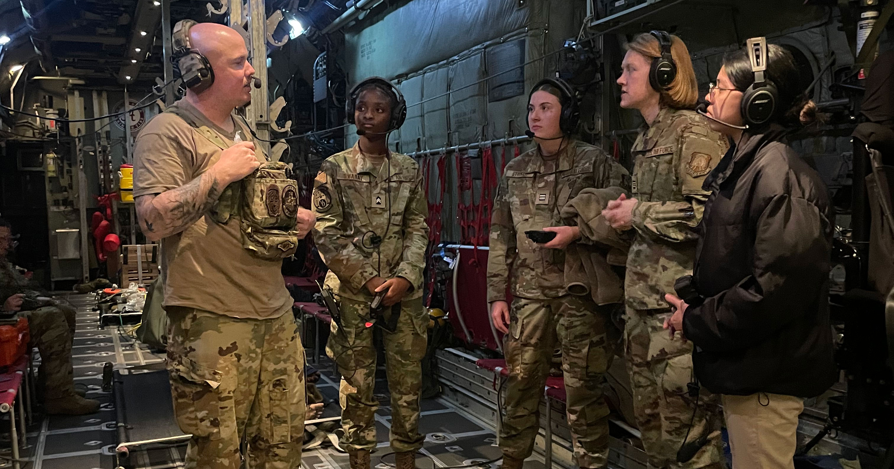 Nursing majors who are cadets in UD Air Force ROTC stand inside a C-130 military aircraft for an aeromedical evacuation simulation. Here, students are shown wearing camouflage and headphones as an instructor speaks with them. 