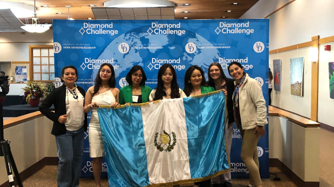 International team poses with flag against the Diamond Challenge banner