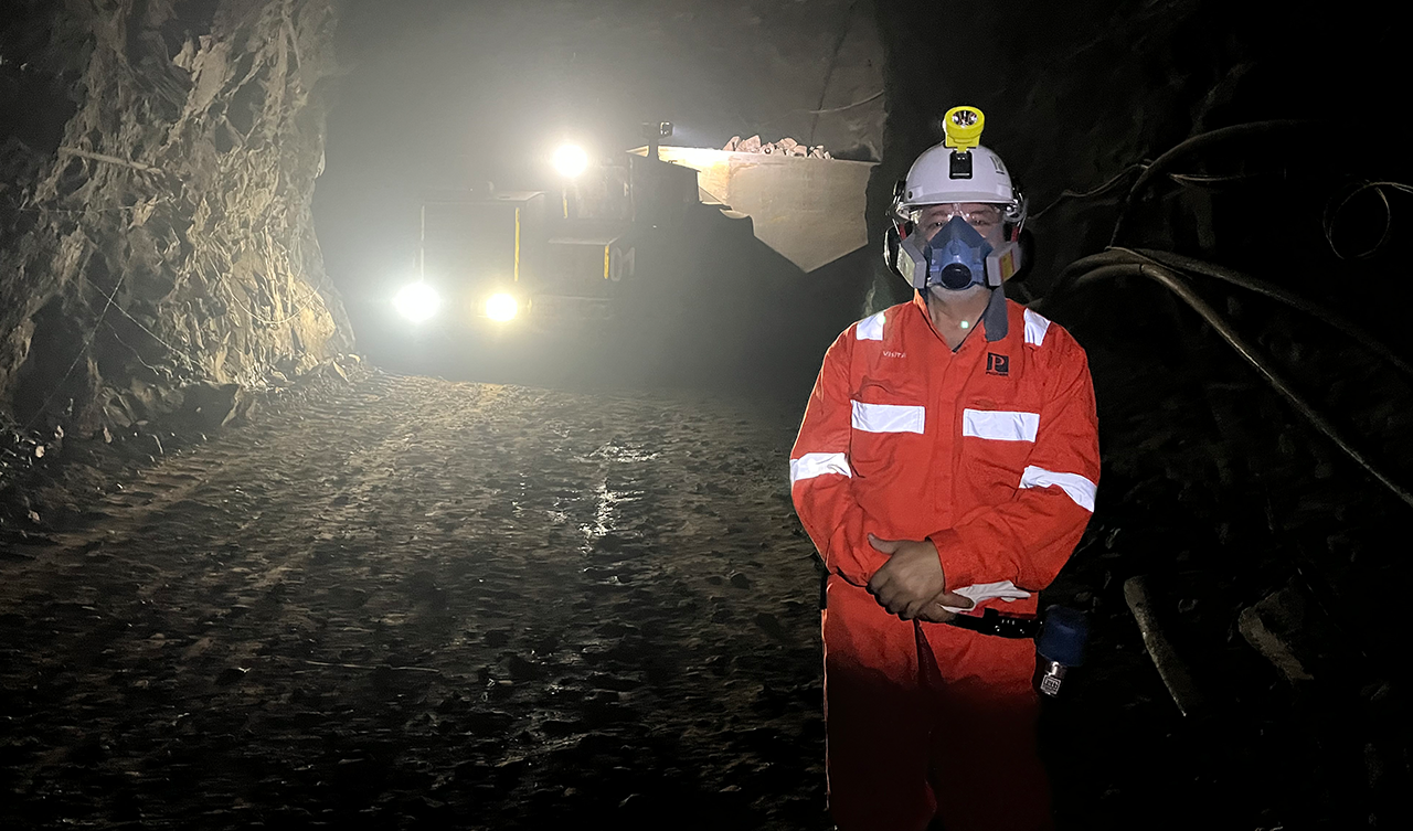 A Fulbright Faculty Scholar in a mine with lights shining from some sort of vehicle in the background.