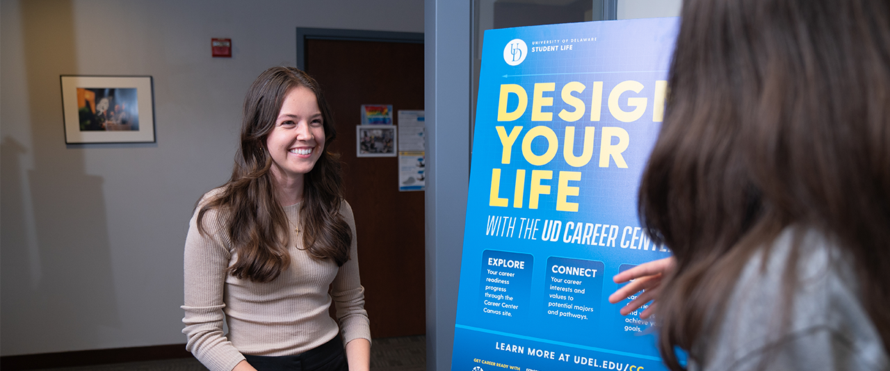 A student speaks with Career Center staff in front of a "Design Your Life" poster