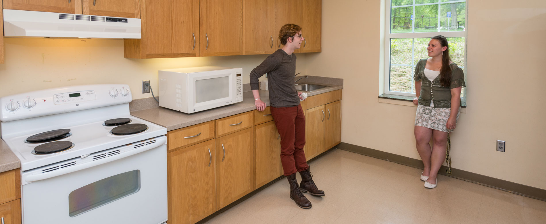 Two students stand and chat in a common kitchen area