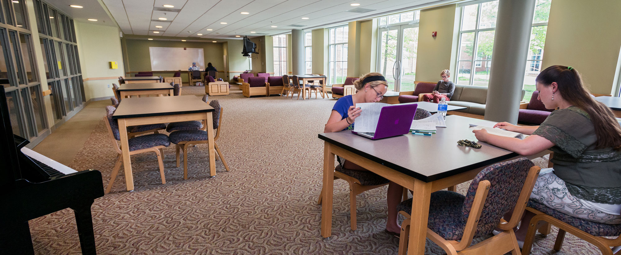 Students studying in a large lounge area with tables and comfortable chairs