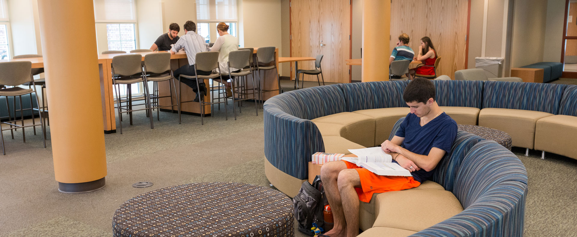 Students studying in lounge with high-top tables, and a curved modular sofa