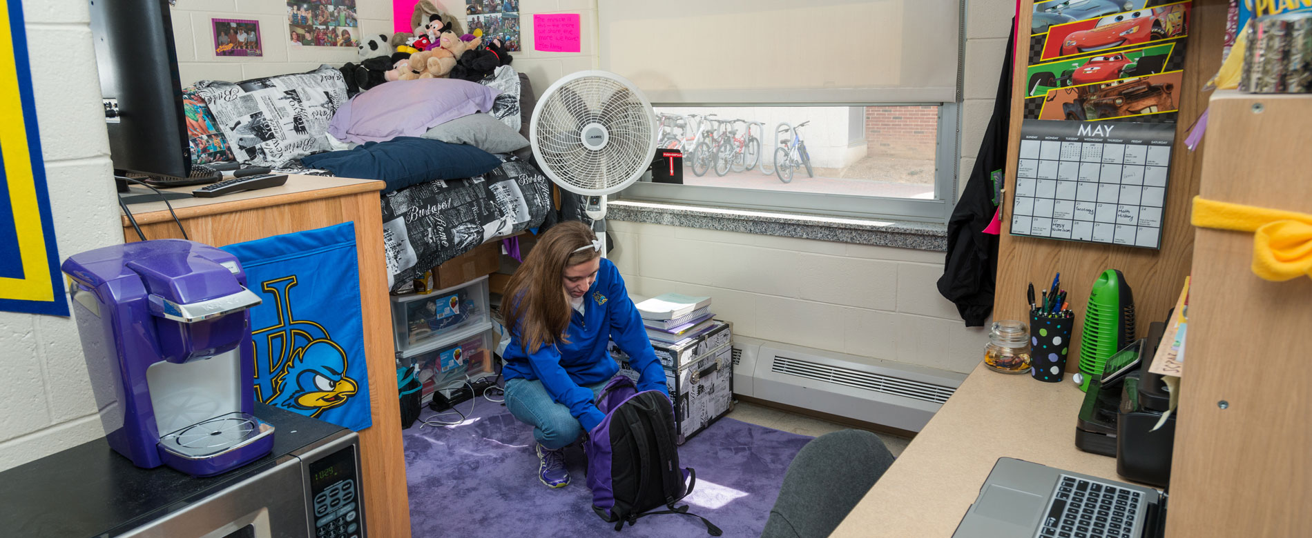 Student kneels and packs a book bag in their room