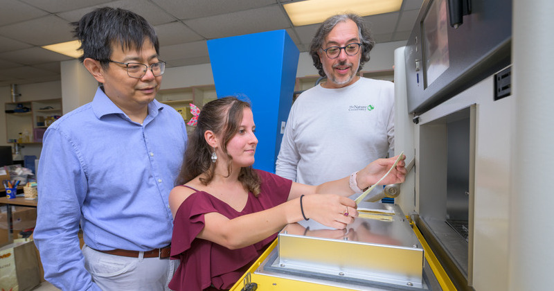 Two professors standing behind grad student holding material