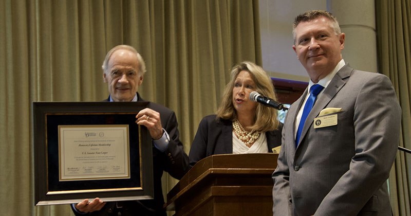 U.S. Sen. (left) holding plaque with 2 UD professors to the right