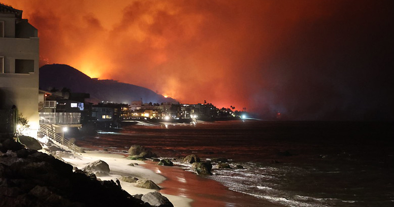 Image of houses on a beach with fire and smoke in the background