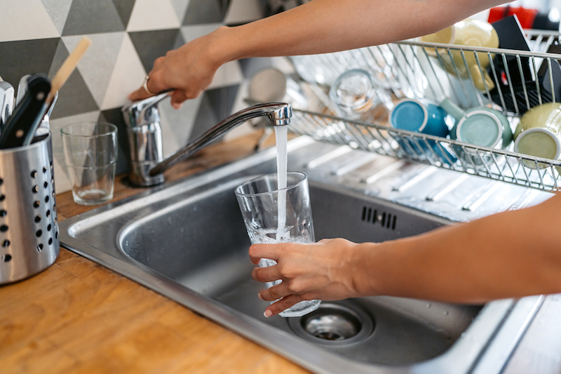 A person is holding a glass of water under a running faucet of a sink