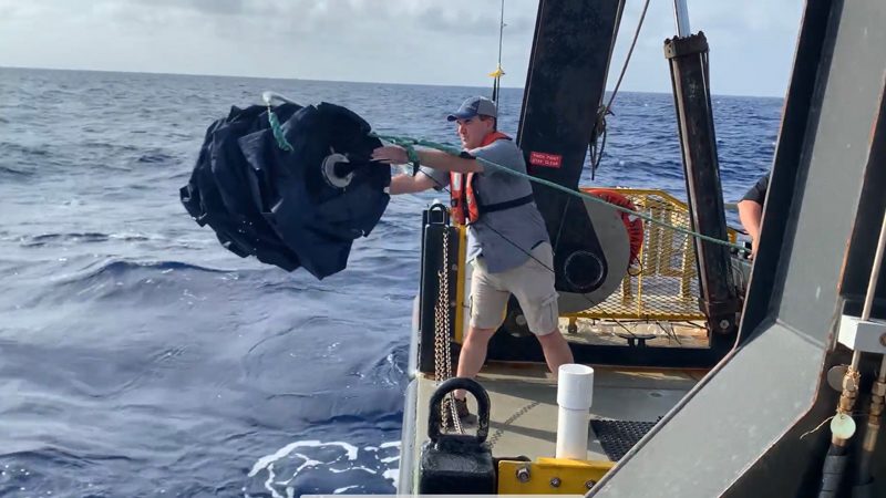 Man on boat retrieving data collection device from water