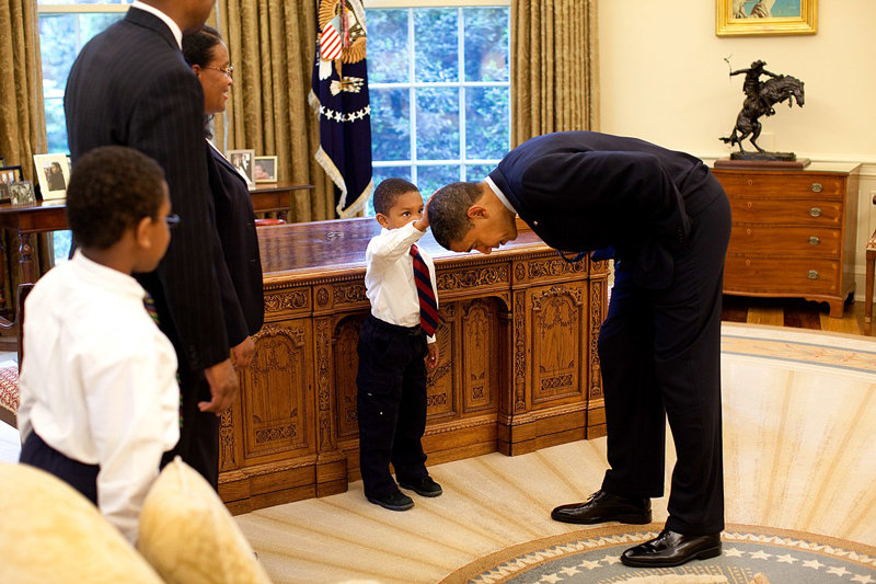 President Barack Obama bends over so the son of a White House staff member can pat his head during a visit to the Oval Office May 8, 2009. Official White House Photo by Pete Souza. This official White House photograph is being made available for publication by news organizations and/or for personal use printing by the subject(s) of the photograph. The photograph may not be manipulated in any way or used in materials, advertisements, products, or promotions that in any way suggest approval or endorsement of the President, the First Family, or the White House.