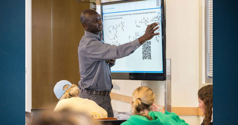 A professor facing a projector screen while teaching   a class