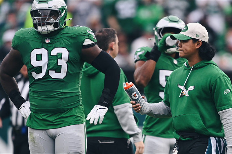 Marco Diaz (right), a seasonal athletic trainer in his first year with the Eagles, ensures players like defensive tackle Milton Williams (left) stay hydrated during a home game against the Dallas Cowboys. (Photo courtesy of Philadelphia Eagles Video Staff.)