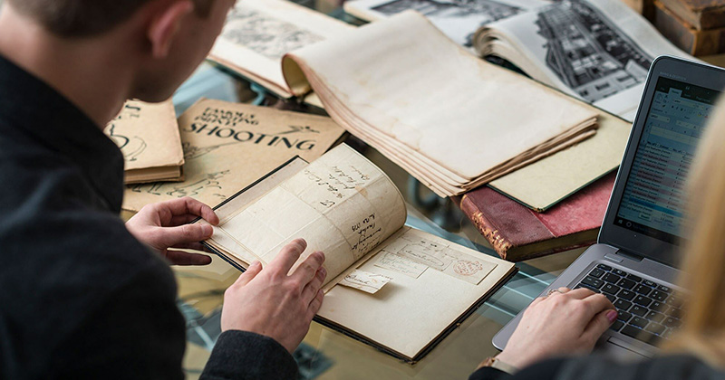 Researchers review special collections materials, vintage books and manuscripts while entering data into a laptop computer.