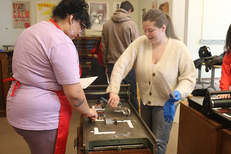 Spring 2025 art graduates Lillyanne Dominguez and Cassidy Driscoll use magnets to keep tiles in place on one of Raven Press’s hand press machines, trying to achieve the “perfect kiss.” Spring 2025 art graduates Lillyanne Dominguez and Cassidy Driscoll use magnets to keep tiles in place on one of Raven Press’s hand press machines, trying to achieve the “perfect kiss.”